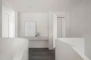 A minimalist bathroom with two concrete bathtubs, dark wooden flooring, and a small shelf with a vase and framed artwork.