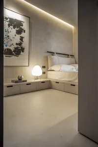 Minimalist bedroom with concrete floor, white bedding, and abstract painting.
