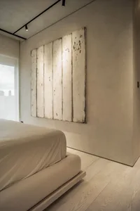 A minimalist bedroom with taupe-colored bedding and a wooden panel wall art