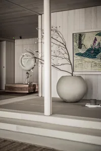 A minimalist interior design featuring a concrete vase with a bare branch and a framed painting hanging on the wall.