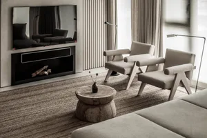 A modern minimalist living room with cushioned furniture, a wooden table, and a flat-screen TV mounted on the wall.