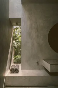 A modern bathroom with concrete walls and a shower area that leads outside to lush greenery.