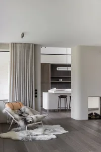 A modern minimalist kitchen with white marble countertops, wooden flooring, and a comfortable lounge area.