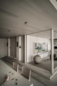 Modern minimalist living room featuring wood flooring and furniture, with a potted plant and abstract painting on the wall.