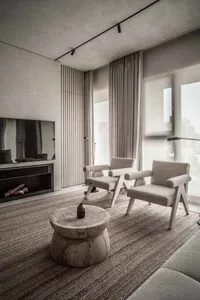 A modern living room with neutral textiles and wooden accents, featuring two armchairs, a coffee table, and a fireplace.