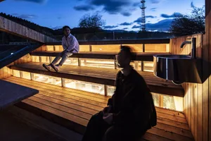 Two people sitting on wooden steps lit by warm lights during sunset.