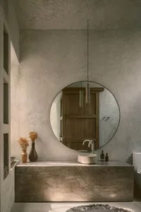 A minimalist bathroom with a black and white color scheme featuring a circular mirror, sink, and vase with dried flowers.