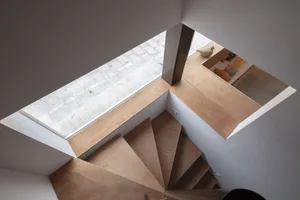 Minimalist interior design featuring a wooden staircase with a skylight and kitchen area.