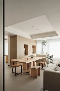 A minimalist living and dining room featuring wood furnishings and soft lighting.