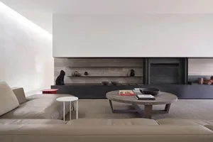 The minimalist living room features a concrete fireplace and wooden coffee table in front of a concrete and wood wall.
