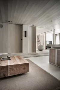 A minimalist living room with a wooden floor, a low wooden coffee table, and a vase with a branch.