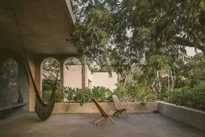 Concrete patio with wooden chairs and a hammock under a large tree