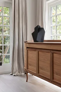 Minimalist sideboard with a hardwood finish, featuring a sculptural black decorative piece and neutral drapes by a window.