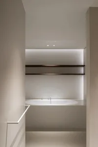 A modern bathroom with a minimalist design, featuring a porcelain-steel bathtub and shelving.