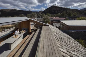 Modern building features a wooden roof with a skylight, set against a backdrop of mountains and cloudy sky.