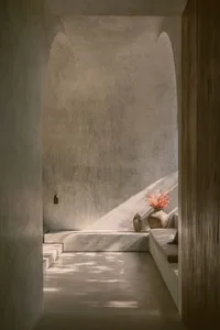 Interior of a minimalist space with concrete walls and floor, featuring a vase with dried flowers and a bench.