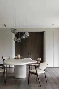 A modern minimalist dining room featuring a concrete and wooden table with white chairs and a glass chandelier.