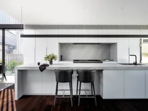 A minimalist kitchen with a concrete countertop, white cabinets, and dark wood flooring.