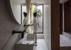 A modern bathroom featuring white tiled walls and floor, a large oval mirror, and a sink with a countertop.
