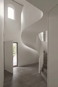 Modern interior design featuring a minimalist concrete staircase with natural light coming through an arched window.