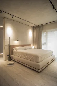 Modern minimalist bedroom with a white bed, white bedding, and motion lights, featuring a white wood floor and a floor lamp.