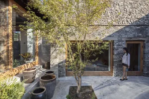 A modern stone house with a courtyard featuring potted plants and a tree.