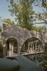 An outdoor living space with a modern design, featuring concrete walls, glass doors, and a pool.