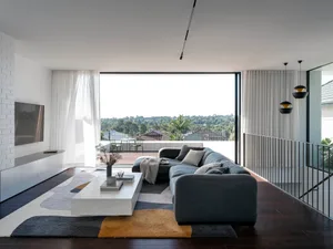A modern living room with a grey sofa, concrete floors, and large windows.