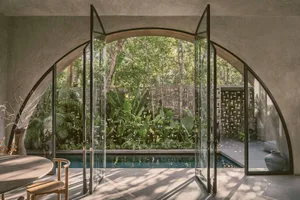 An elegant indoor residential pool surrounded by glass walls with lush greenery outside.