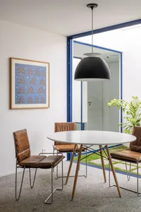 An industrial dining room featuring a wooden table and chairs, with a black pendant light and a blue-framed window.