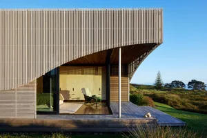 A modern, minimalist residential exterior featuring wood and glass materials, with a view of the surrounding landscape.