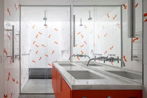A modern bathroom with white and orange tiles, a double sink vanity, and a glass-enclosed shower.