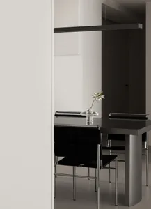 Minimalist dining room with black chairs and metallic table, featuring a single white flower in a glass vase.