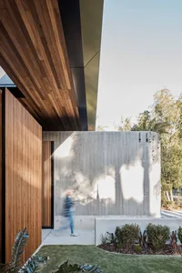 A modern residential entryway featuring a wooden door and a concrete wall with a large, illuminated window.