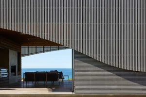 Modern villa exterior featuring a wooden veranda with seating overlooking the ocean.