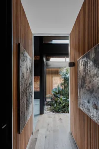 A modern interior hallway with wooden paneling, a small garden space with plants, and abstract art hanging on the walls.