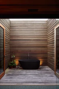 Contemporary bathroom with sleek black bathtub, wooden paneling, and plants set on a wooden floor.