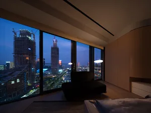 A modern, minimalist bedroom featuring a glass window overlooking a cityscape at dusk.