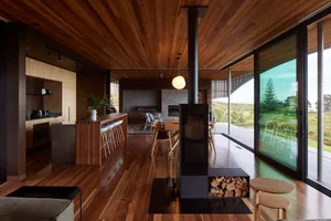 Modern residential kitchen with wooden flooring and ceiling, featuring a central fireplace and an outdoor view.