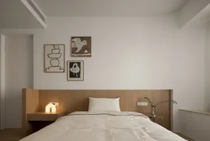 A minimalist bedroom with a wooden bed frame, white bedding, and three framed artworks on the wall.