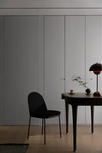 Minimalist office space featuring a black chair next to a minimalist desk with a lamp and a small plant.