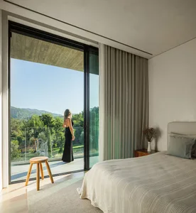 A modern bedroom with a glass door providing a view of greenery outside, featuring a canvas window treatment and a single woo