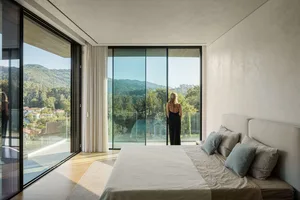 A modern bedroom with large glass windows overlooking green hills.