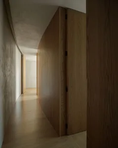 A minimalist hallway with curved wooden panels, natural light, and smooth walls.
