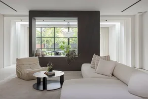 A modern living room with white soft textiles, minimalist furniture, and a view of the garden through large windows.