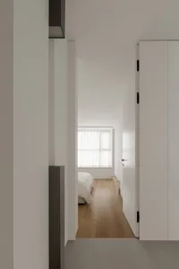 A minimalist bedroom with wood flooring and a bed.