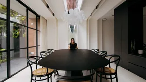 Modern meeting room with black wooden table and metal chairs, featuring plants and artistic lighting fixture.