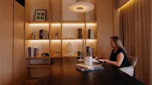 A woman works in a minimalist workspace with wooden elements and warm lighting.