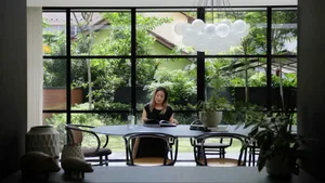 A modern home office featuring a round dining table with metal and glass chairs surrounded by plants, set against a backdrop 