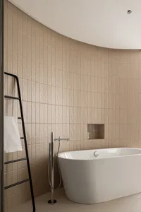 A minimalist bathroom with tiles and a concrete bathtub, featuring a black ladder and a recessed shelf.